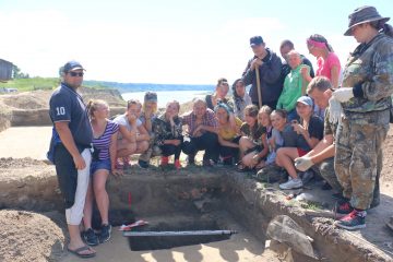 Группа школьников и студентов позирует у раскопа на фоне Иртыша.